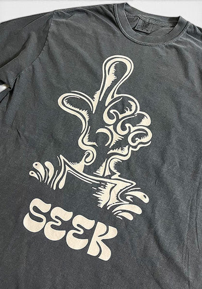 SEEKのDEGARASHIコラボTシャツ。ヴィンテージ風のチャコールグレーのコットンボディにユニークなグラフィックがプリントされています。